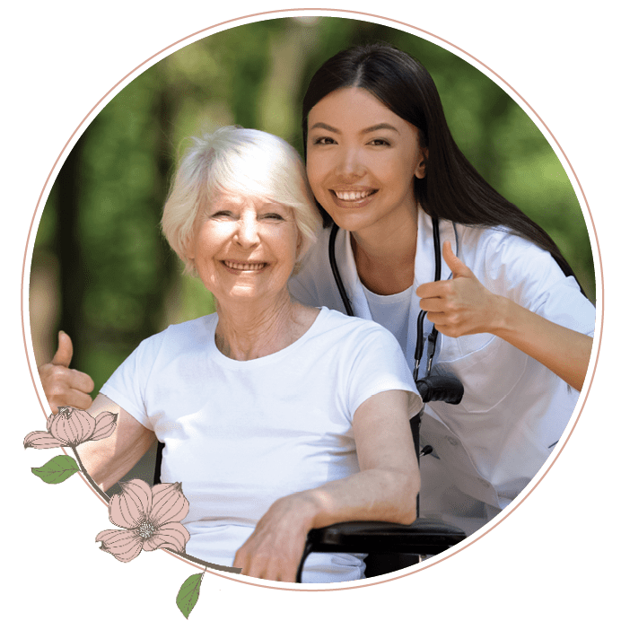 A nurse standing next to an elderly woman in a wheelchair giving a thumbs up