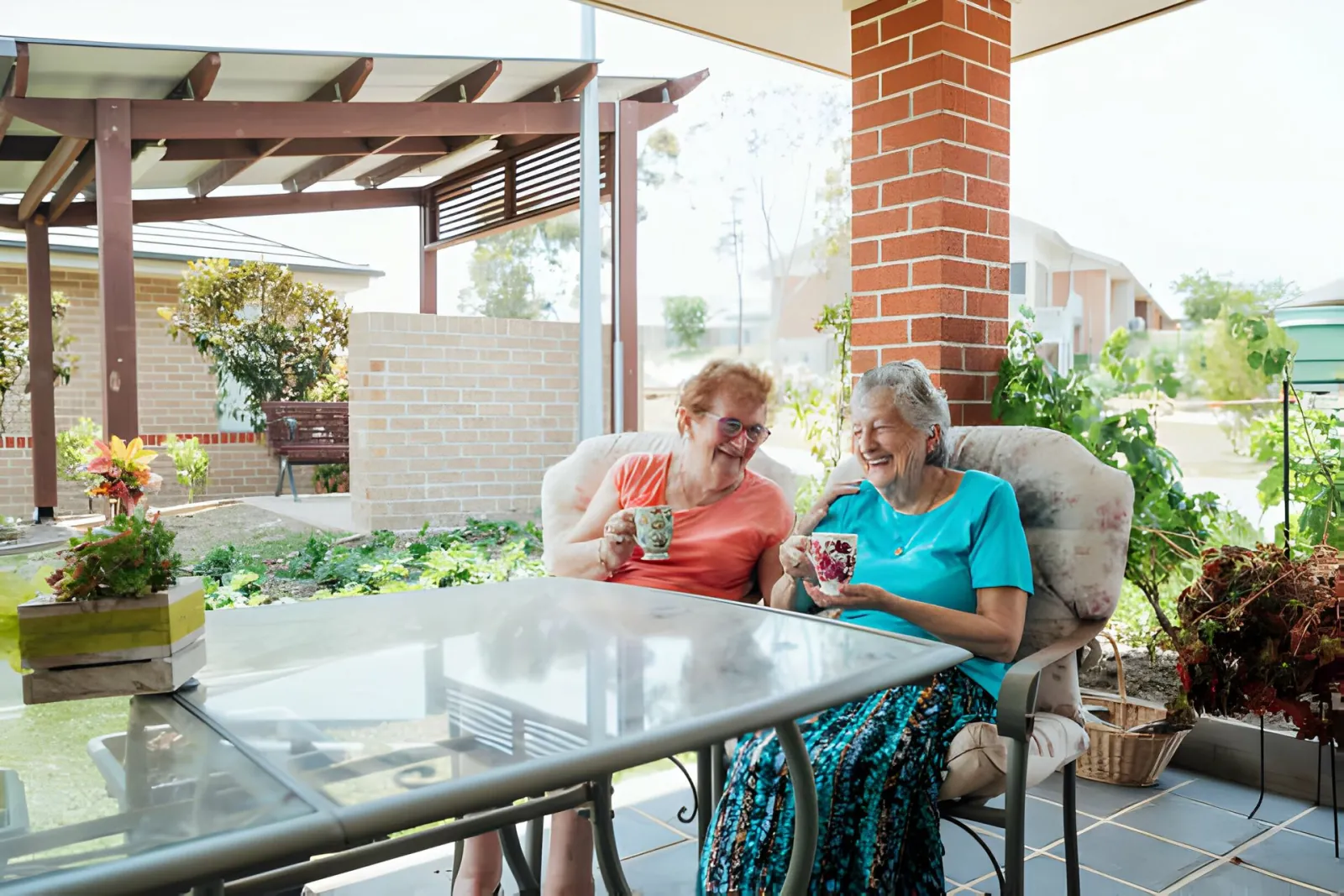 Two older women sitting at a table on a porch drinking coffee