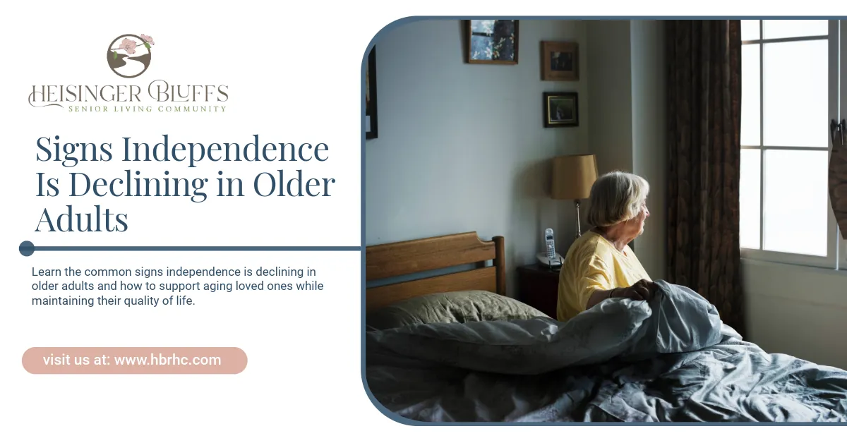 An older adult is sitting on the bed, looking out the window. 